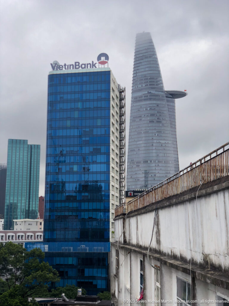 Bitexco Financial Tower behind a blue VietinBank building and elevated concrete structure.