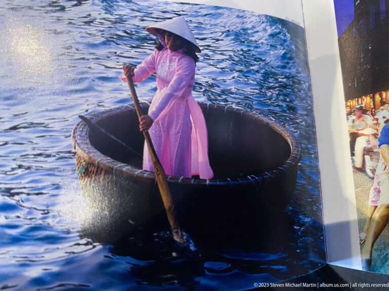 Displayed image of a woman in pink paddling a round basket boat on blue water.
