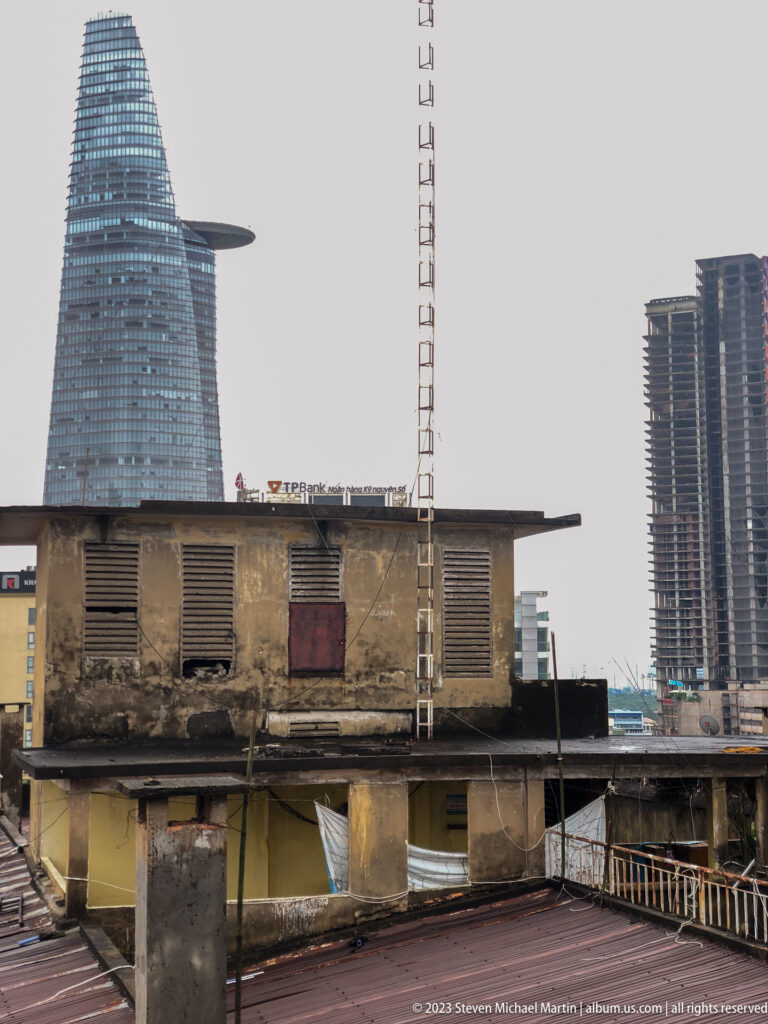 Weathered rooftop building in front of Bitexco Financial Tower and modern high-rises.