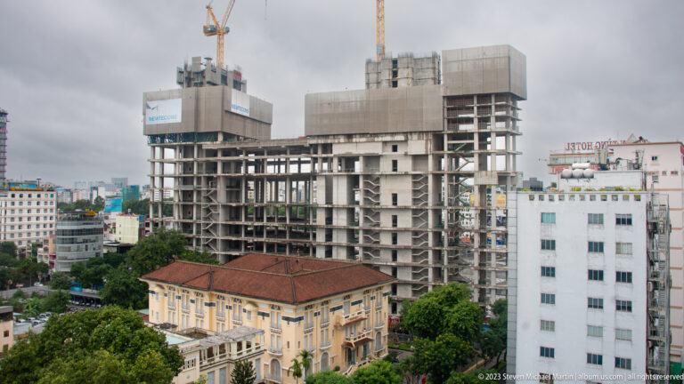 Red-roofed historic hotel in front of a large unfinished concrete high-rise construction site.