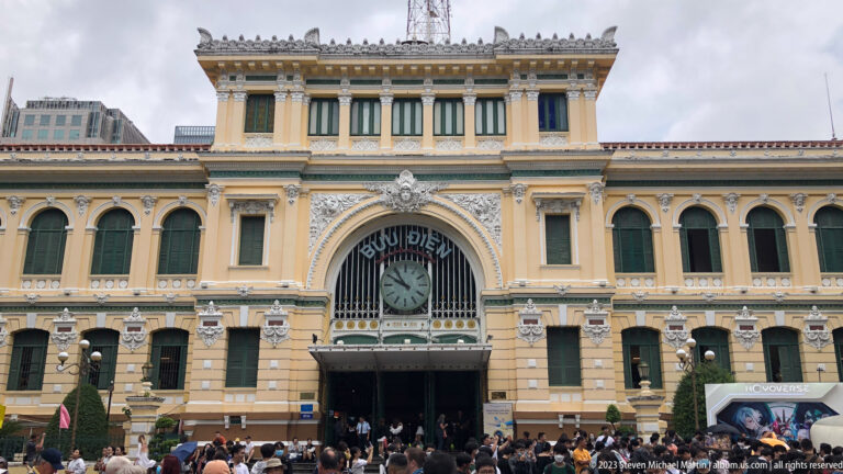 Front façade of Saigon Central Post Office with central clock and visitors.