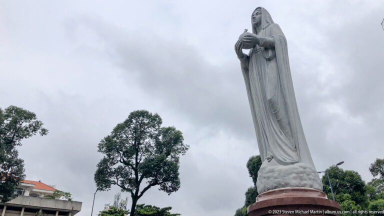 White statue of the Virgin Mary above trees.