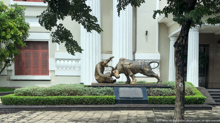 Bronze bull sculpture before a white-columned building.