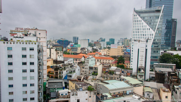 White angular high-rise above dense low-rise buildings and mixed modern towers in Ho Chi Minh City.
