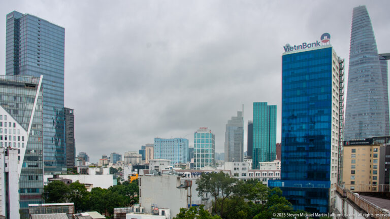 Bitexco Financial Tower and blue VietinBank building above lower rooftops and trees in Ho Chi Minh City.