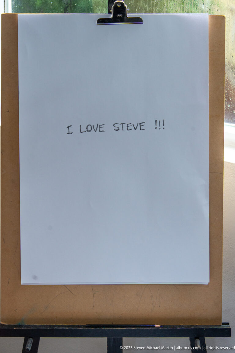 White paper on a wooden easel bears the handwritten message “I LOVE STEVE!!!” in black ink.