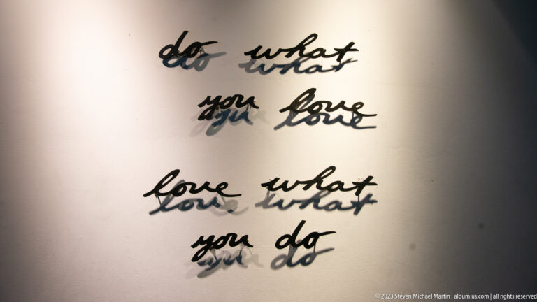 Black script wall quote reading “do what you love, love what you do,” with strong cast shadows.