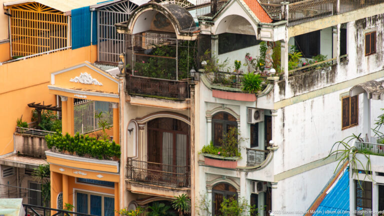 Orange and white residential façades with arched balconies, decorative trim, potted plants, and weathered plaster.