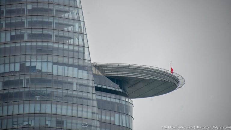 Close detail of Bitexco Financial Tower’s projecting helipad, curved glass façade, and small Vietnamese flag.