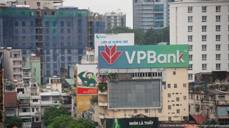 Large green VPBank sign above dense commercial buildings, billboards, and rooftops in Ho Chi Minh City.