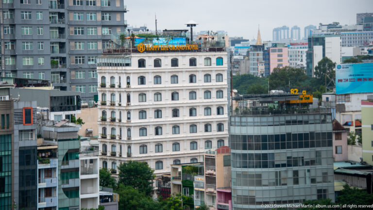 White multi-story hotel with repeated arched windows among modern commercial towers and rooftop signs.