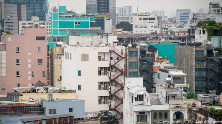 Dense cluster of pastel and concrete mid-rise buildings with external stairs, terraces, and rooftop additions.