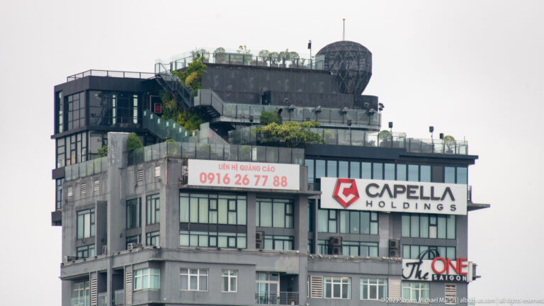 Commercial building with CarePlus Holdings and The One Saigon signs, rooftop greenery, antennas, and a large spherical structure.