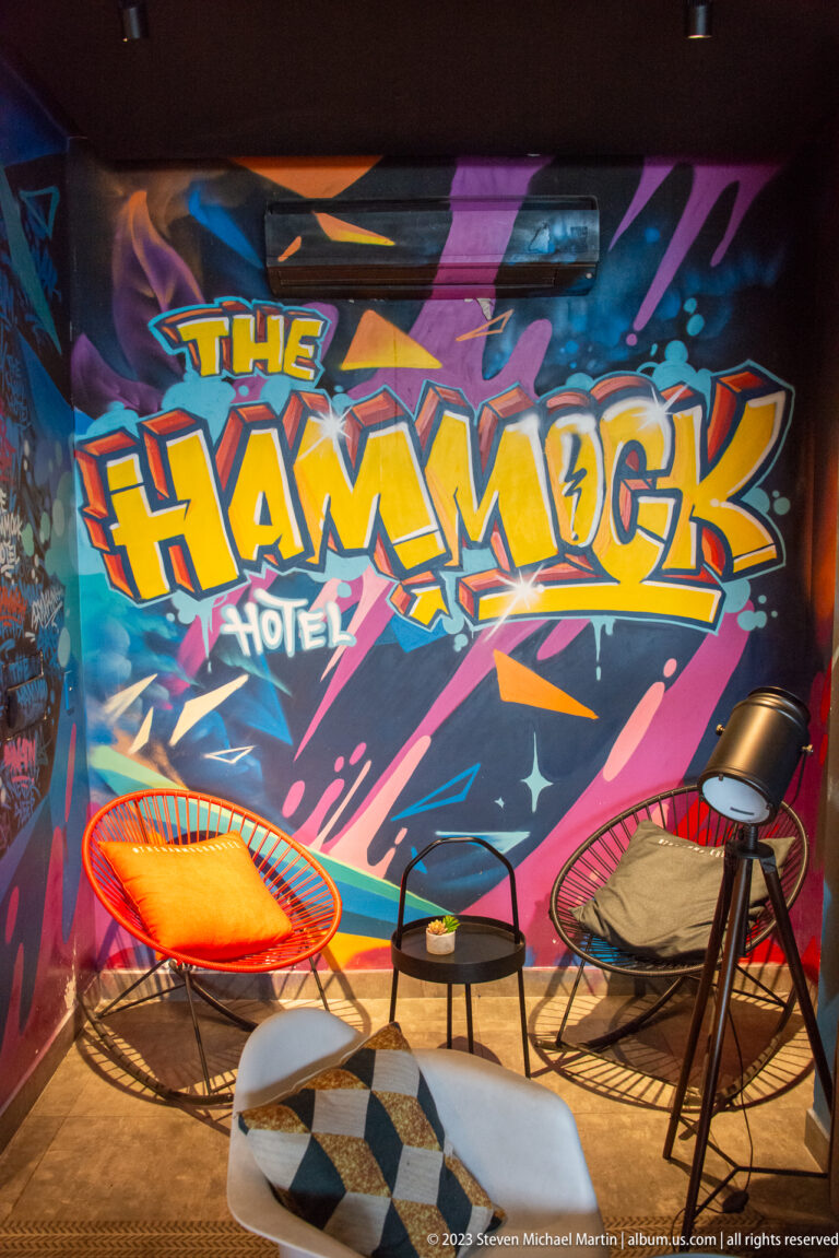 Colorful Hammock Hotel graffiti mural behind lounge chairs, small tables, and a patterned rug.