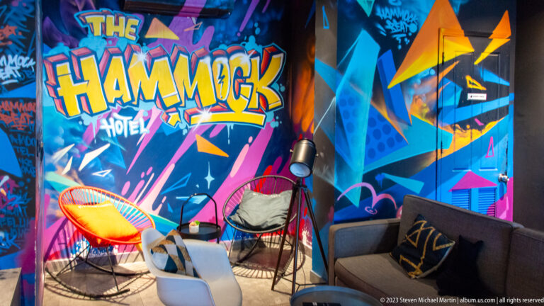 Colorful Hammock Hotel lounge with graffiti mural, wire chairs, sofas, small tables, and hanging lights.