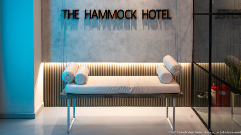 Pale bench with cylindrical cushions beneath The Hammock Hotel sign and a warm horizontal light strip.