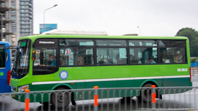 Green SaigonBus route 31 carrying passengers along a divided city roadway.