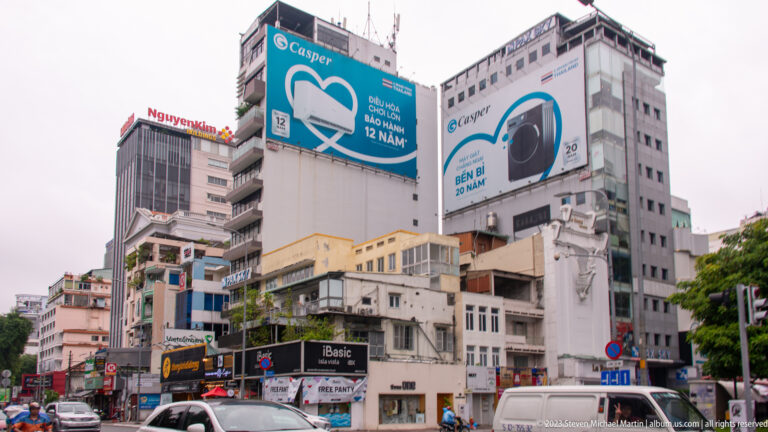Large Casper air-conditioner billboard above layered commercial buildings and traffic in central Ho Chi Minh City.