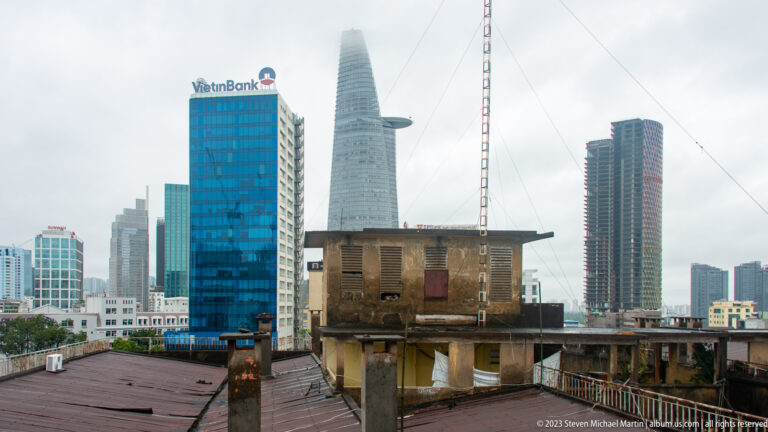 Weathered rooftop house in front of modern Ho Chi Minh City towers, including the tapered Bitexco Financial Tower.