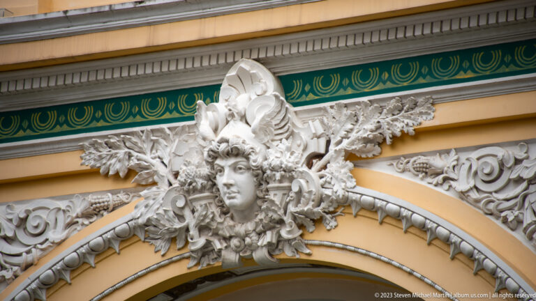 White sculpted female head with radiating floral scrollwork on the yellow-and-green façade of Saigon Central Post Office.