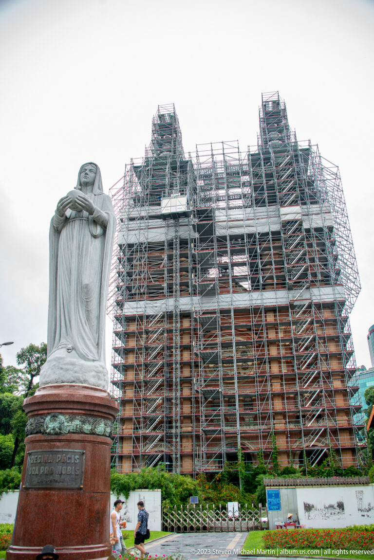 Statue of Our Lady of Peace on a red pedestal before Notre-Dame Cathedral Basilica of Saigon covered in scaffolding.