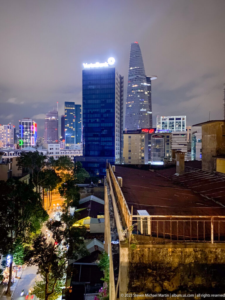 Night skyline of Ho Chi Minh City with Bitexco Financial Tower beyond older rooftops.