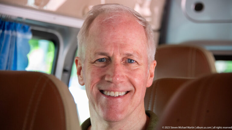 Smiling older man seated in a tan leather vehicle interior.