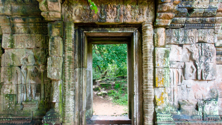 Doorway framed by carved stone opening onto bright forest at Angkor Thom.