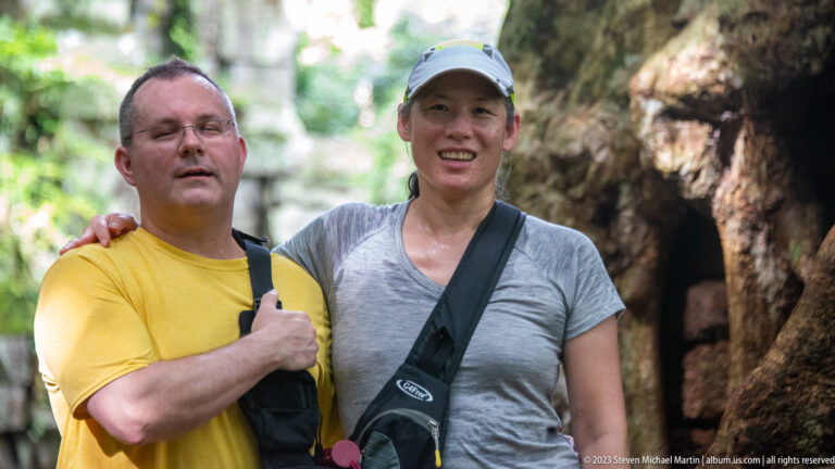 Close portrait of two visitors beside giant tree roots at Angkor Thom.