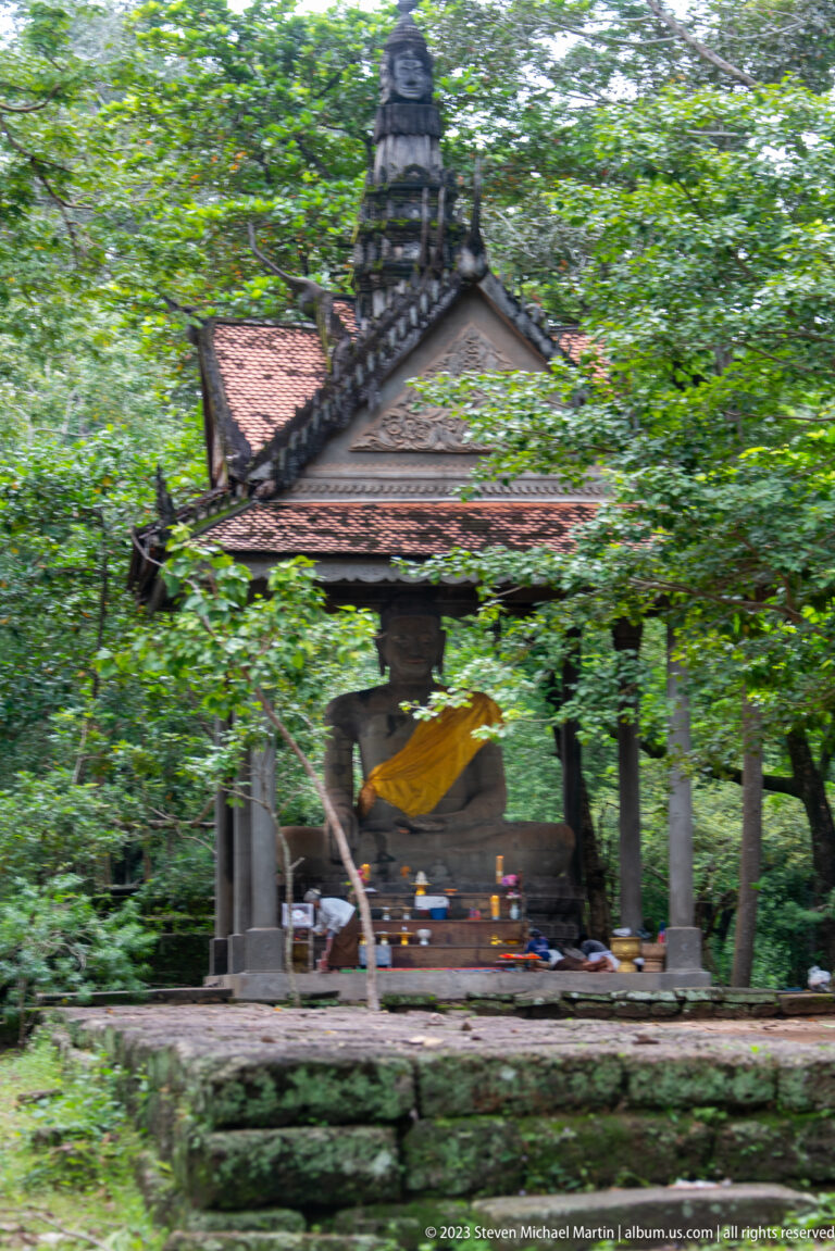 Small roofed shrine sheltering a seated Buddha draped in yellow cloth at Angkor Thom.