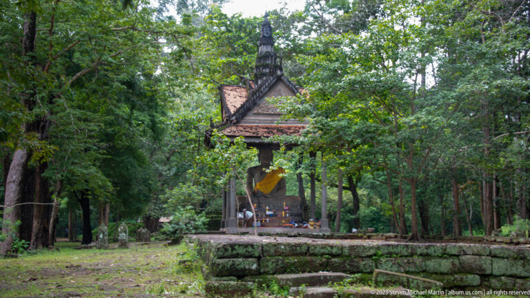 Wider view of the yellow-draped Buddha shrine on a raised platform at Angkor Thom.