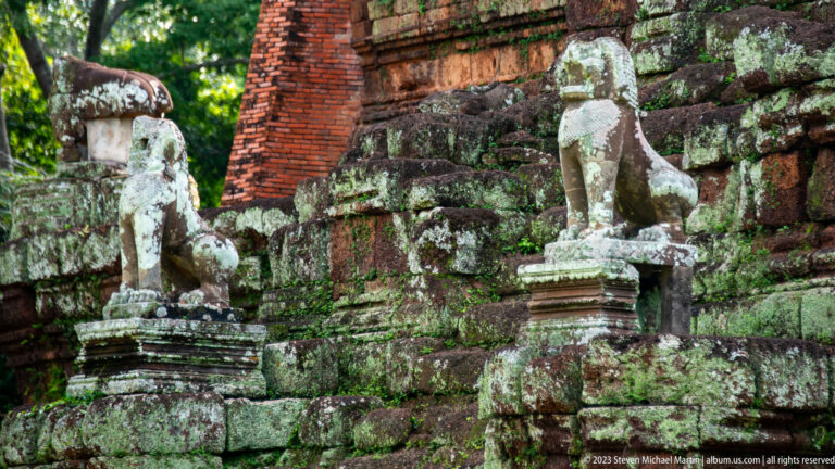 Pair of weathered guardian lions beside red brick masonry at Angkor Thom.