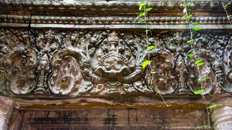 Close sandstone lintel with curling foliage and central face at Angkor Thom.