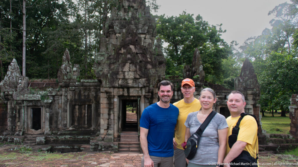 Four visitors posing with more of the gateway visible at Angkor Thom.