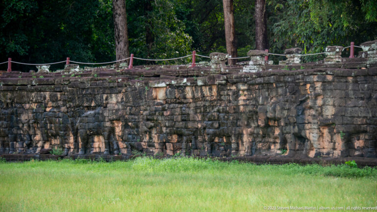 Long elephant-carved terrace wall across bright grass at Angkor Thom.