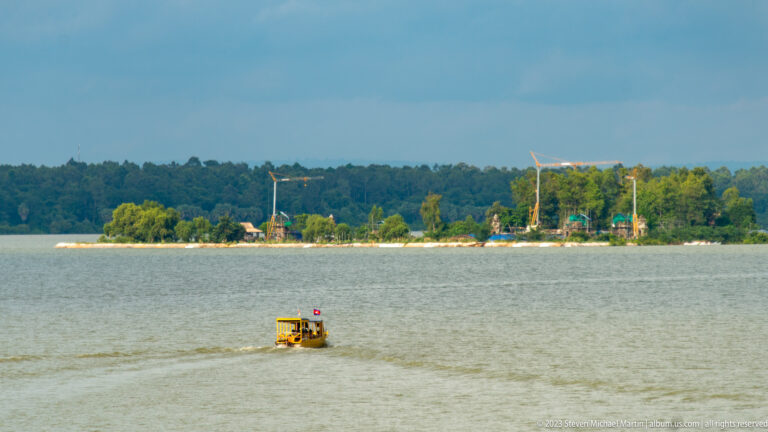 Small boat on broad reservoir with wooded shoreline at Angkor Thom.