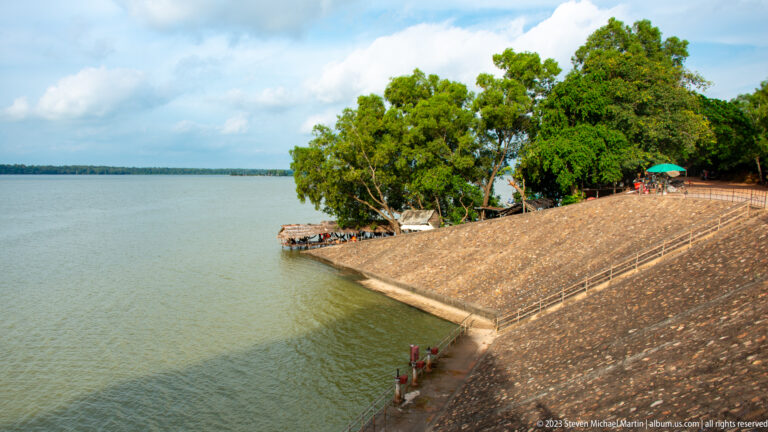 Stone embankment and green trees beside blue-green water at Angkor Thom.