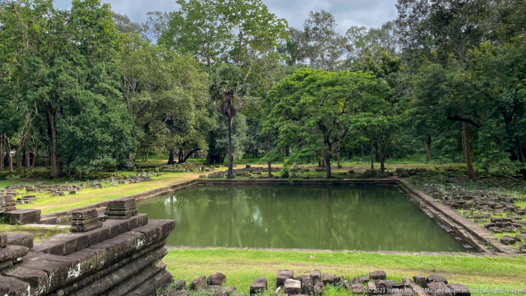 Rectangular stone-lined pond surrounded by lawn and trees at Angkor Thom.