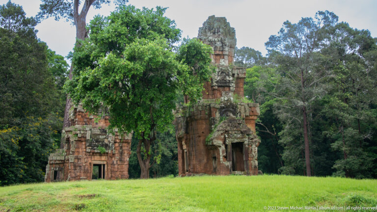 Tall reddish gateway tower standing alone in grass at Angkor Thom.