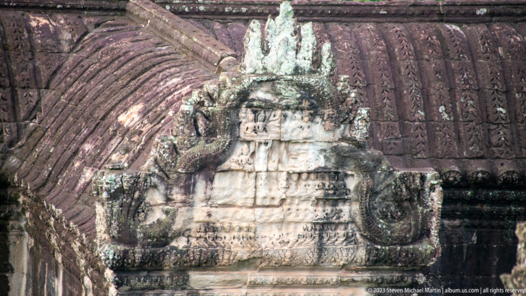 Weathered triangular pediment with a central sacred figure and curling side forms at Angkor Wat.