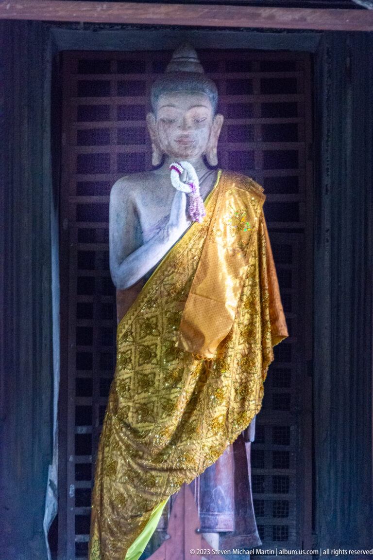 Standing Buddha statue draped in gold cloth inside a dark doorway at Angkor Wat.