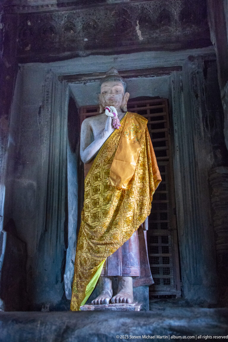 Three-quarter view of the gold-draped Buddha framed by the doorway at Angkor Wat.