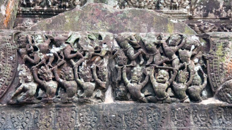 Horizontal frieze of many small dancing or struggling figures above an inscription band at Angkor Wat.