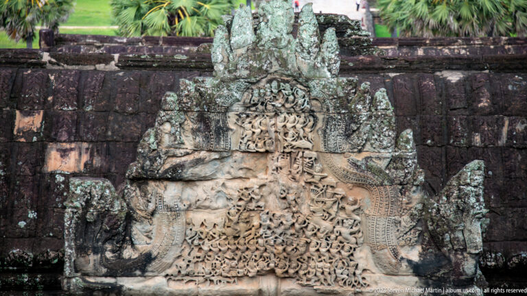 Weathered pediment packed with rows of small figures beneath a central crest at Angkor Wat.