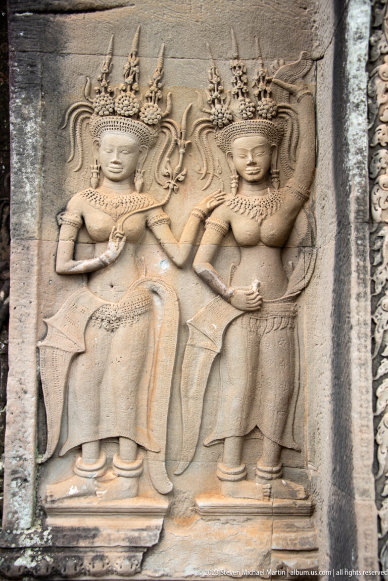 Close pair of standing devatas with jewelry and one raised hand at Angkor Wat.