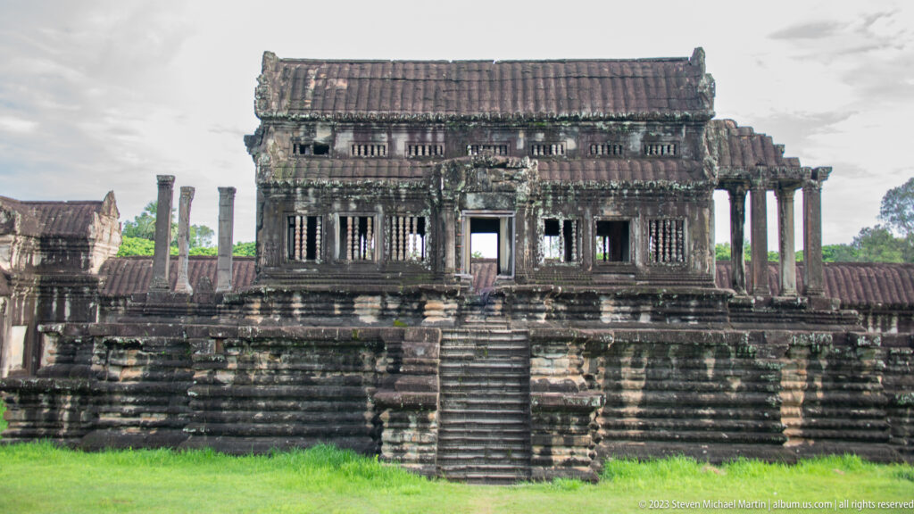 Long dark temple façade with central stair, rows of columns, and raised platform at Angkor Wat.