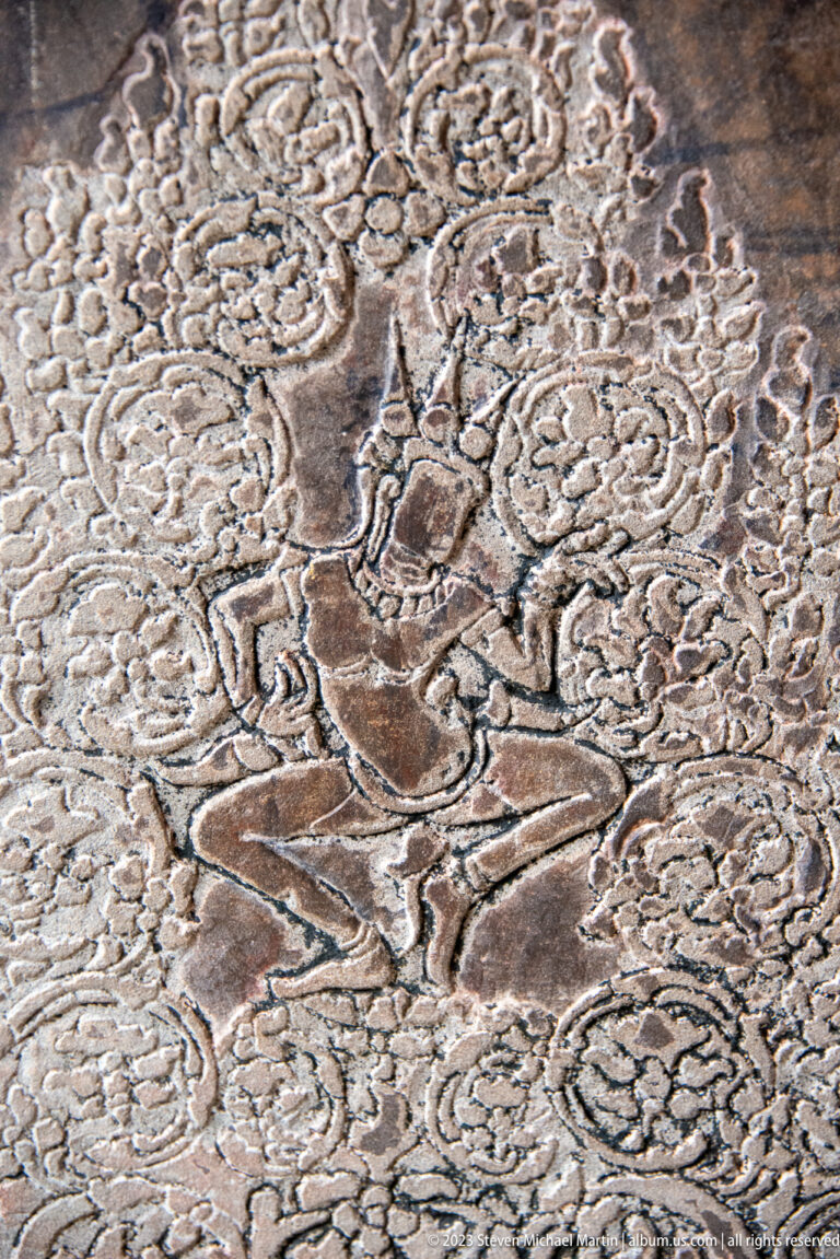 Dynamic figure with arms raised amid curling floral or cloud-like ornament at Angkor Wat.