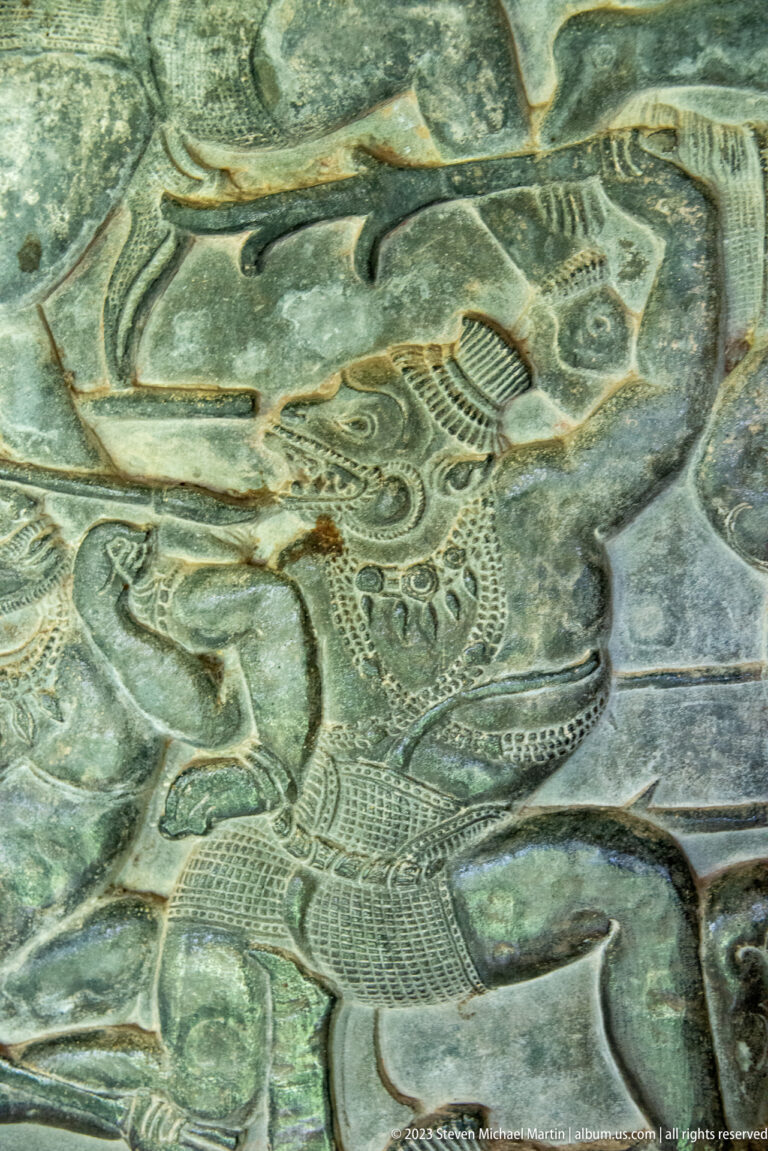 Close animal-headed or helmeted figure with patterned body and open mouth at Angkor Wat.