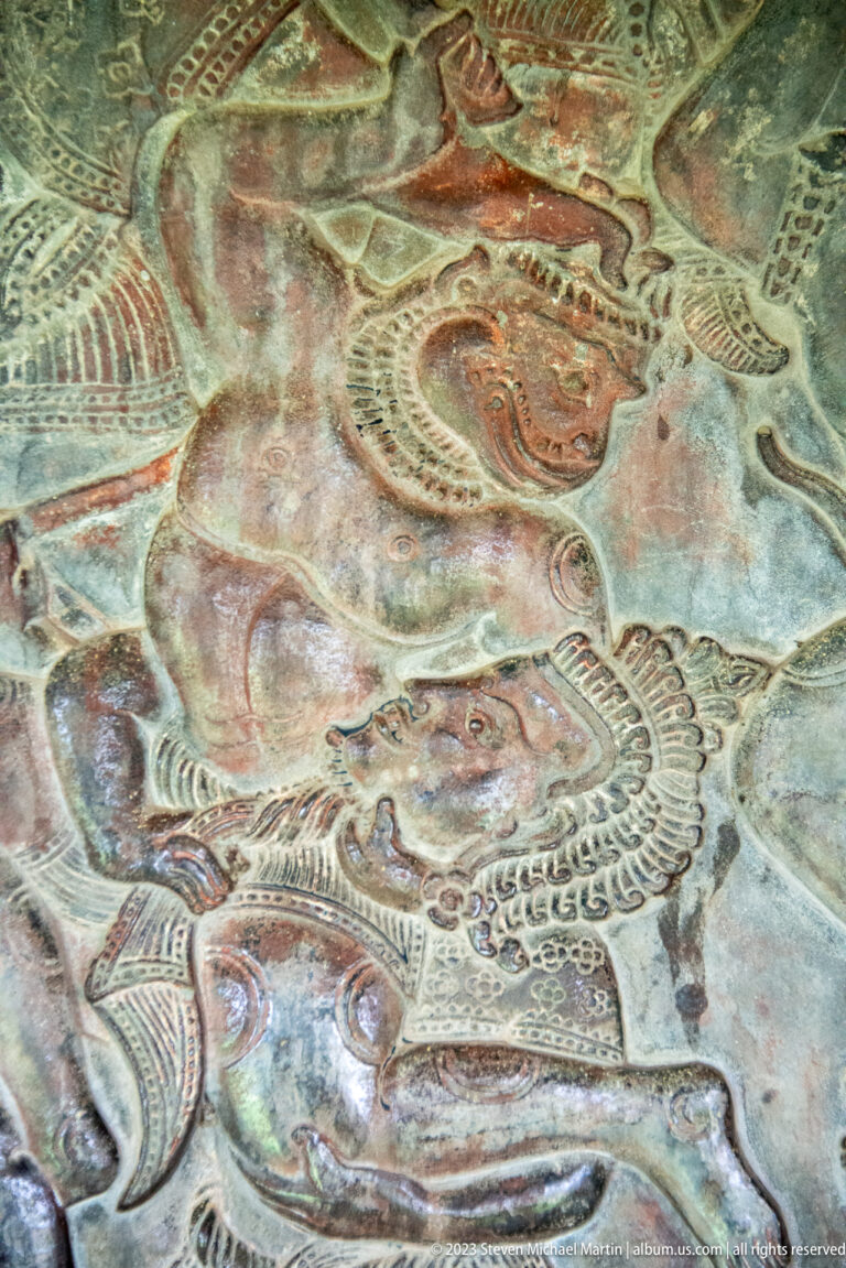 Colored relief of a large face or creature beside another figure at Angkor Wat.