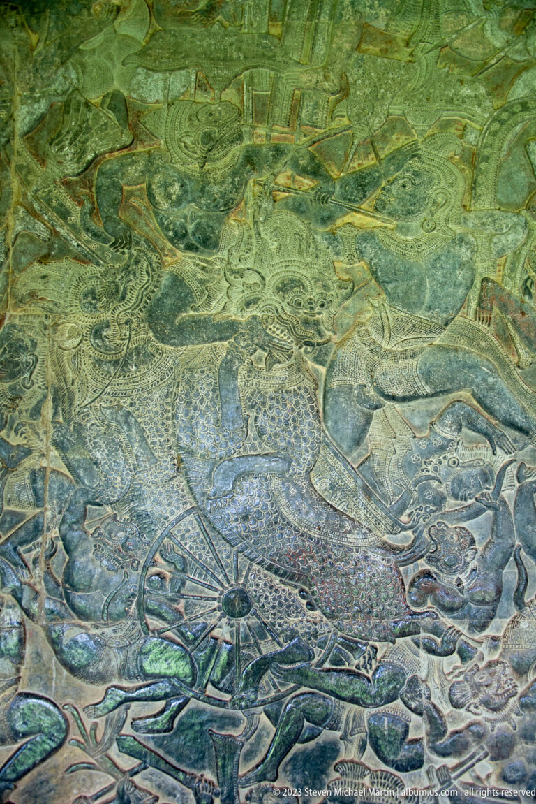 Faint relief with a large central figure, animals, and curling background forms at Angkor Wat.